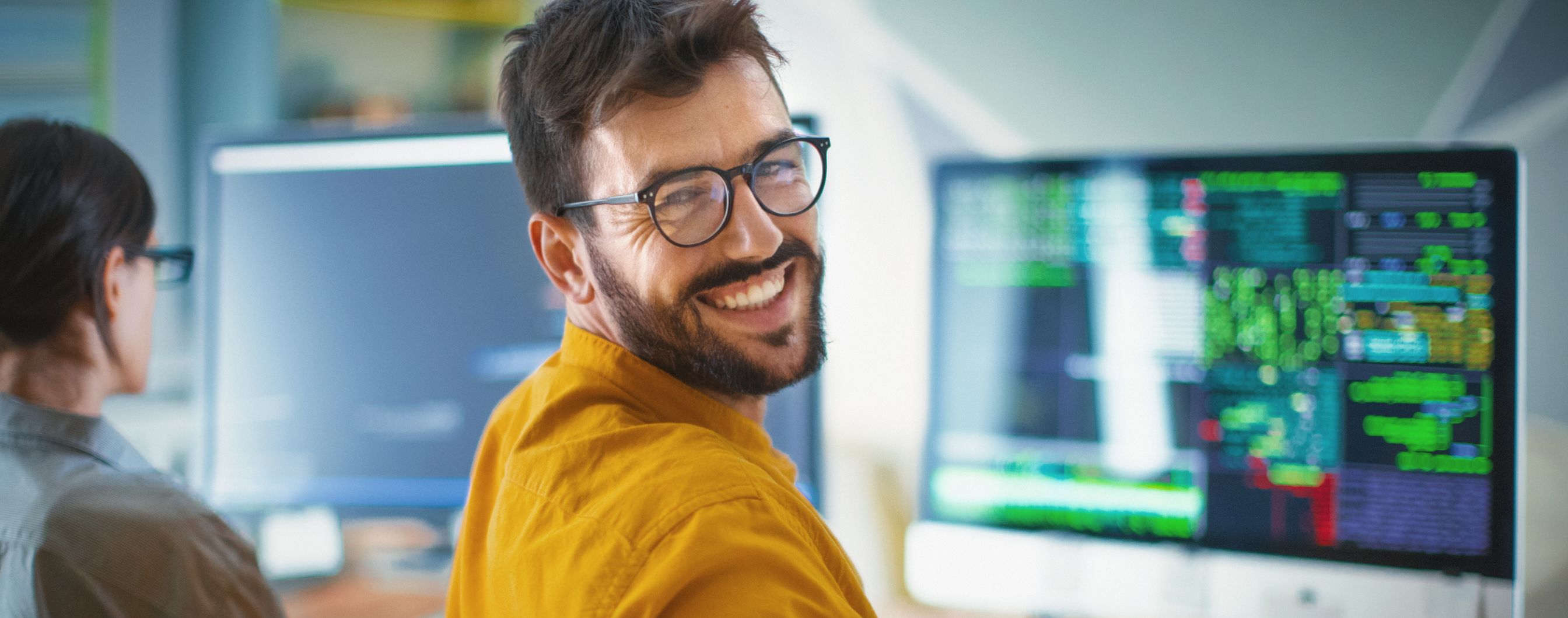 developer IT w okularach uśmiecha się, komputer w tle